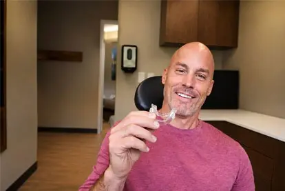 Smiling man holding a clear oral sleep apnea appliance in a dental office